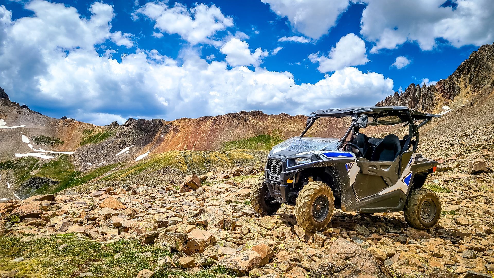 Side-by-side ATV on a rocky mountain trail under a blue sky with clouds.