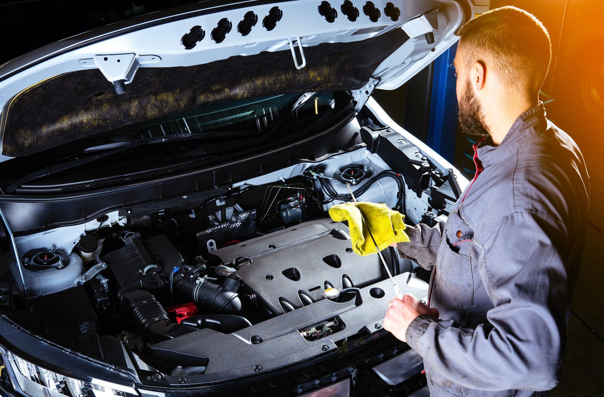 Mechanic inspecting car engine with yellow cloth, garage setting.