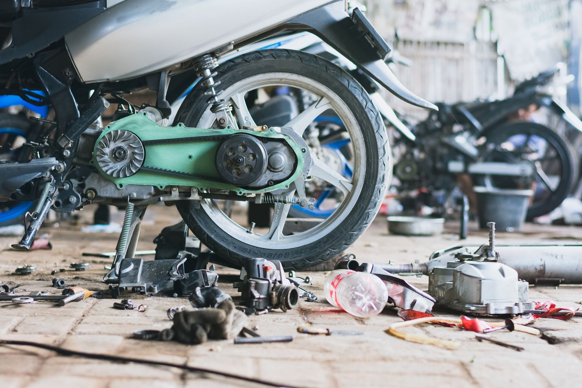 Motorcycle being repaired in a garage, surrounded by tools and parts on the floor.