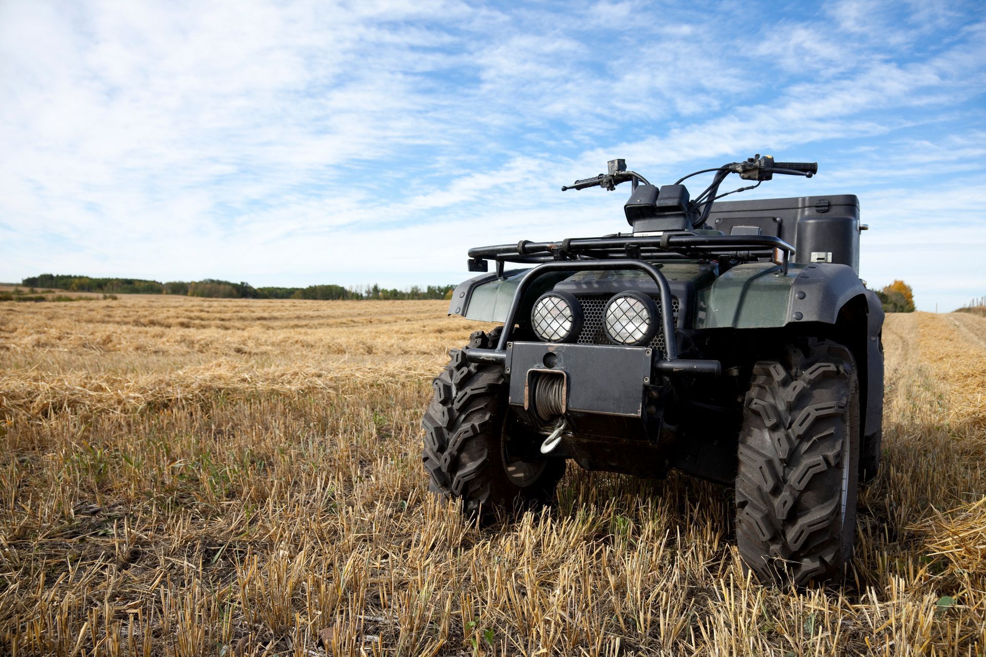ATV parked in a harvested field under a blue, cloudy sky.