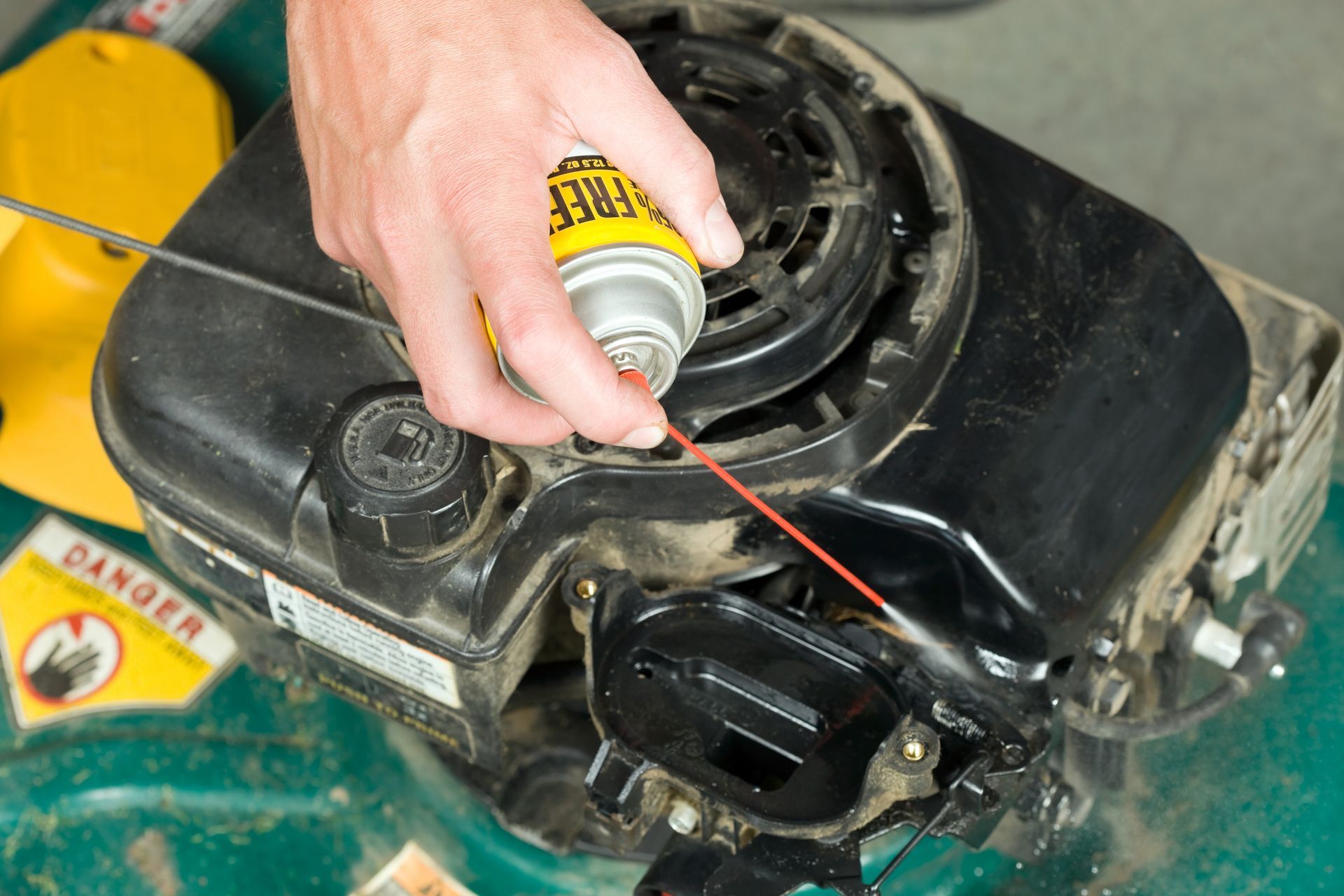 Person sprays lubricant on a lawnmower engine.