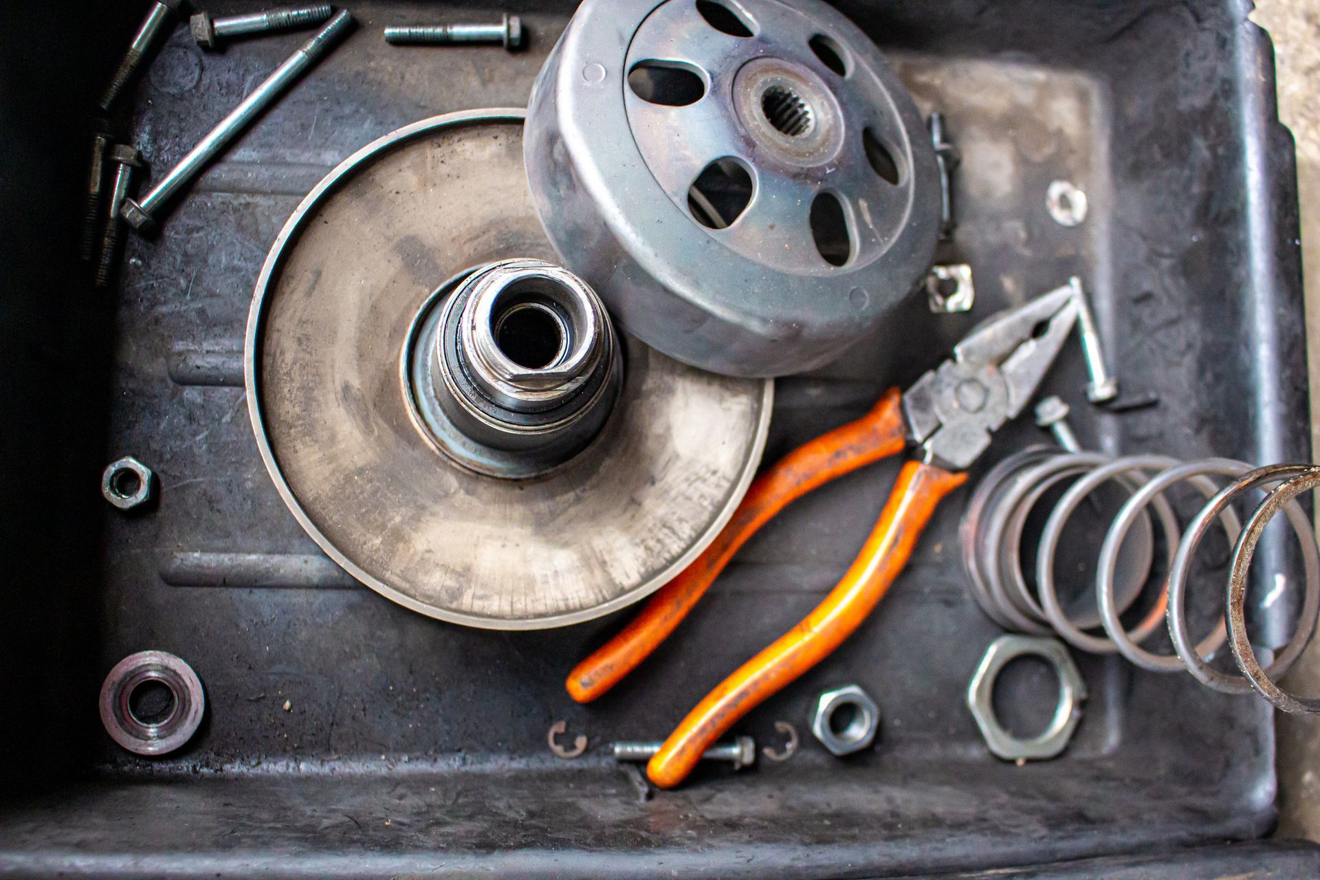 Mechanical parts and pliers in a black tray, likely scooter or motorcycle repair.
