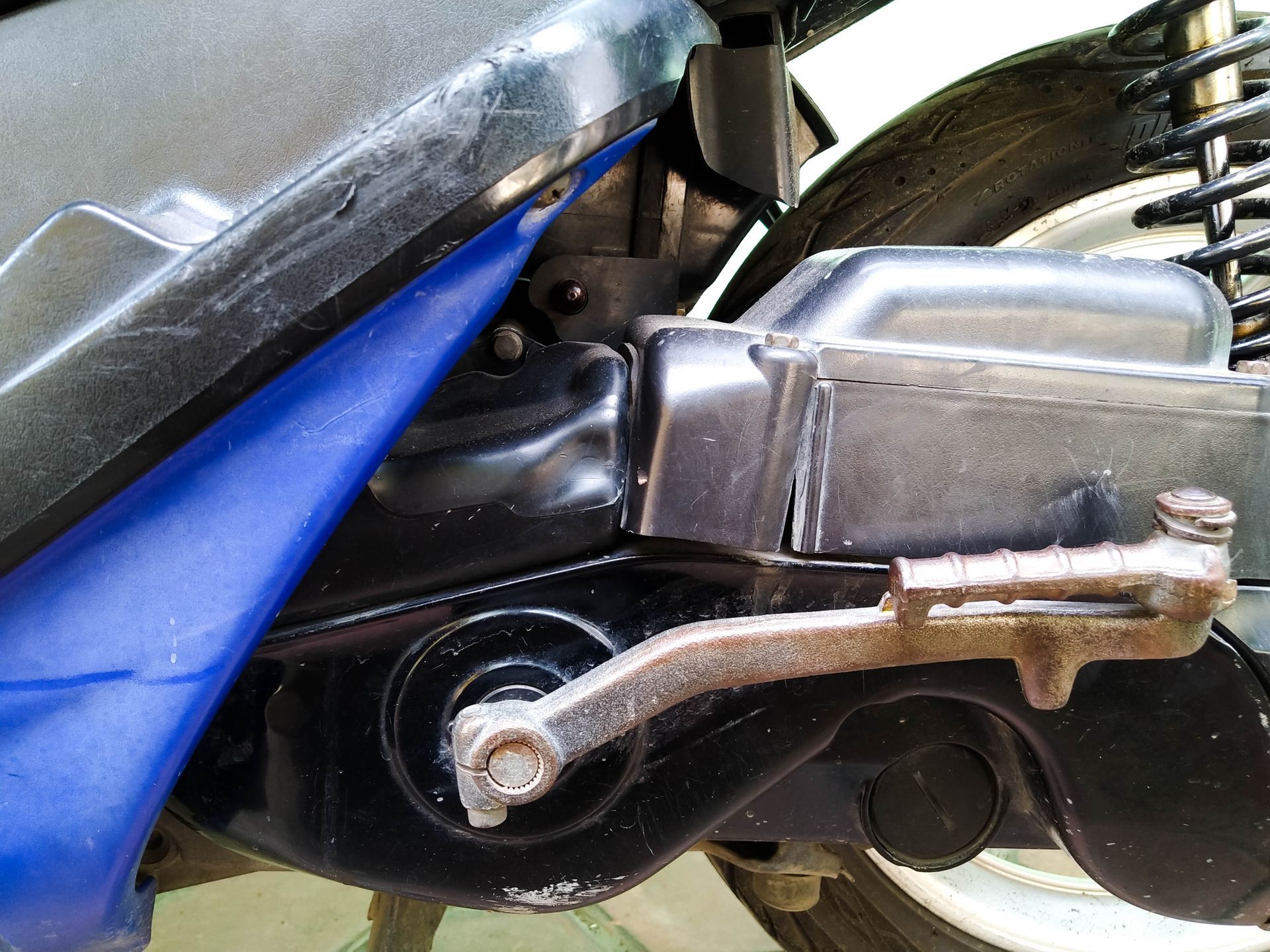 Close-up of a scooter engine with a black and blue body, showing the kickstart lever and other components.