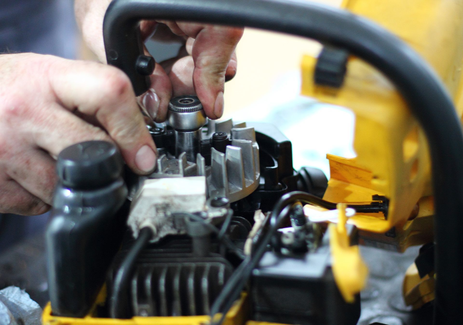 Hands assembling a chainsaw engine, in a close-up shot. Yellow and black chainsaw parts are visible.