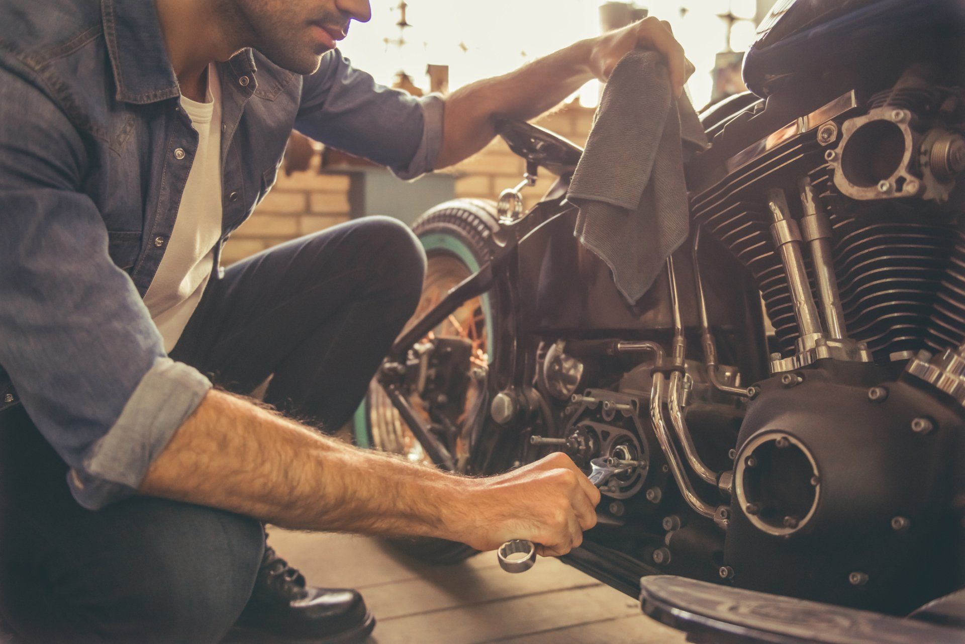 Man in a garage working on a motorcycle, wiping parts with a rag.