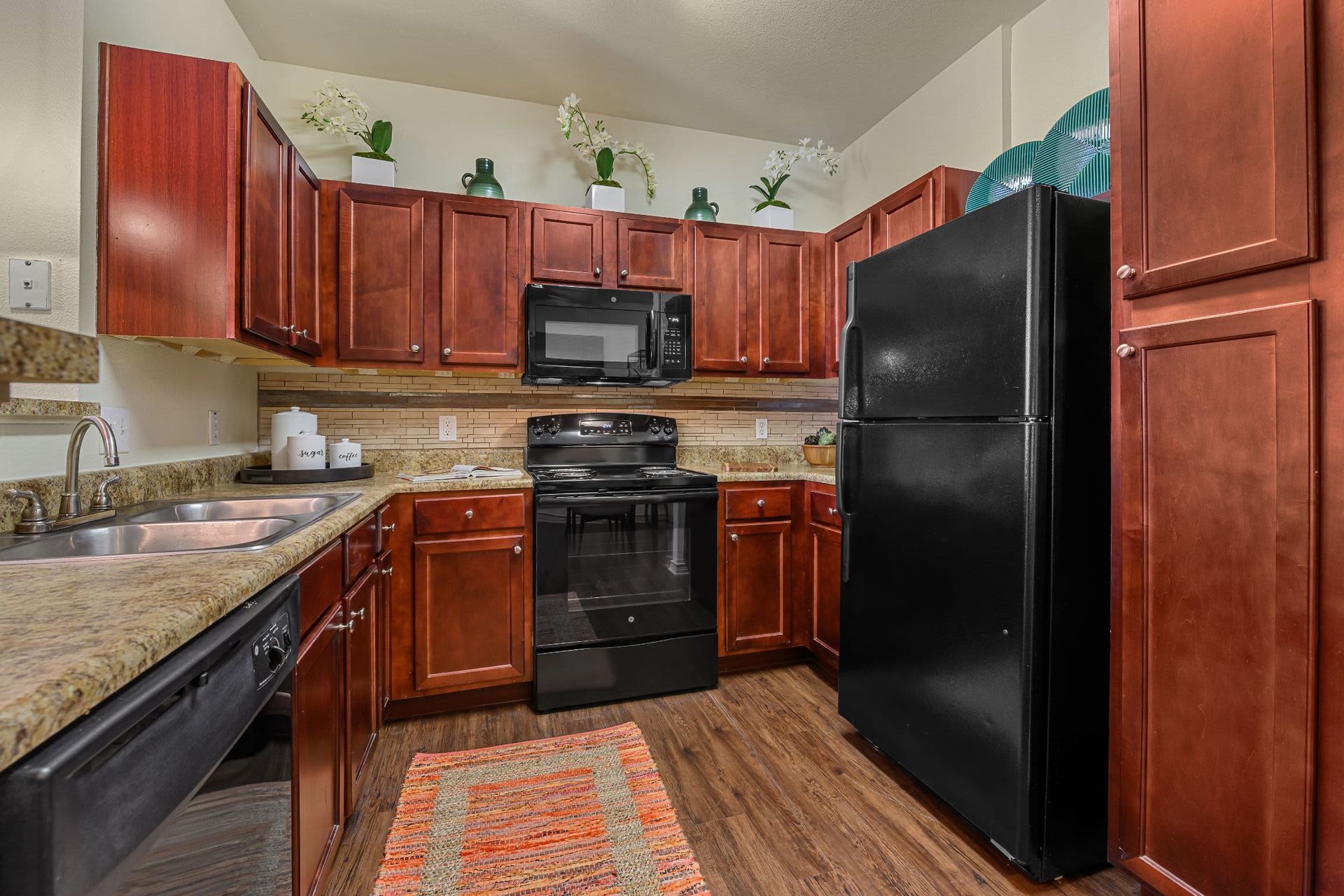 A kitchen with wooden cabinets, a black refrigerator, a stove, a microwave, and a sink at Marquis Lakeline Station in Austin, TX.