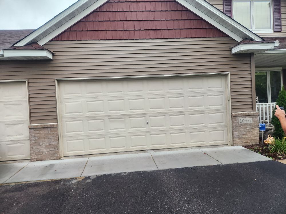 A person is standing in front of a house with a garage door open.