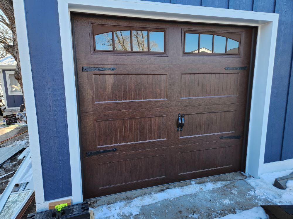 A wooden garage door is sitting in front of a blue house.