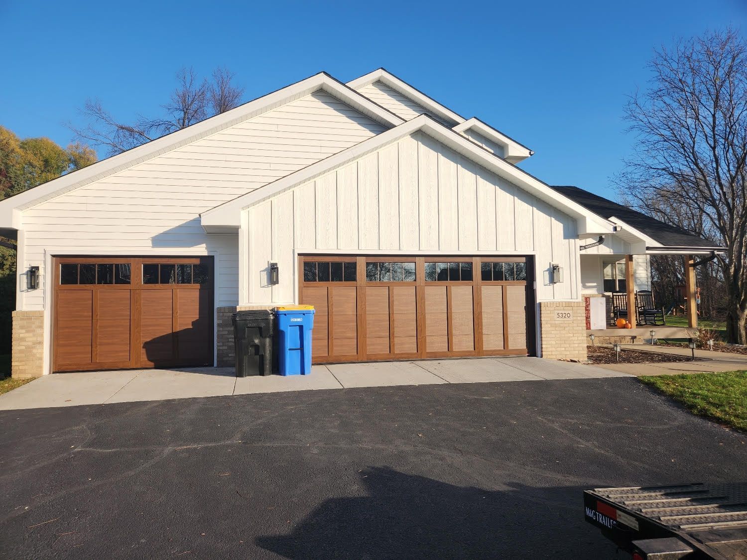 A white house with brown garage doors and a blue trash can