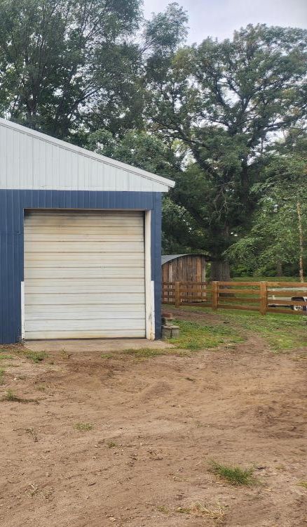A blue and white garage with a white garage door in a dirt field.