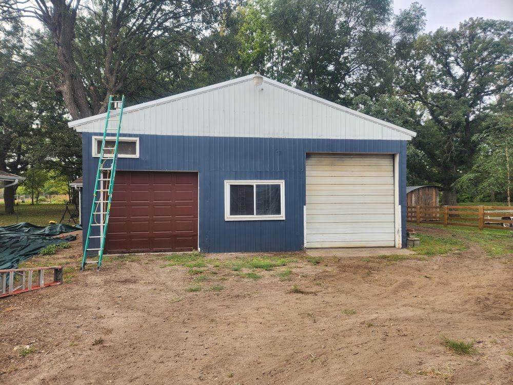 A blue and white garage with a ladder in front of it.
