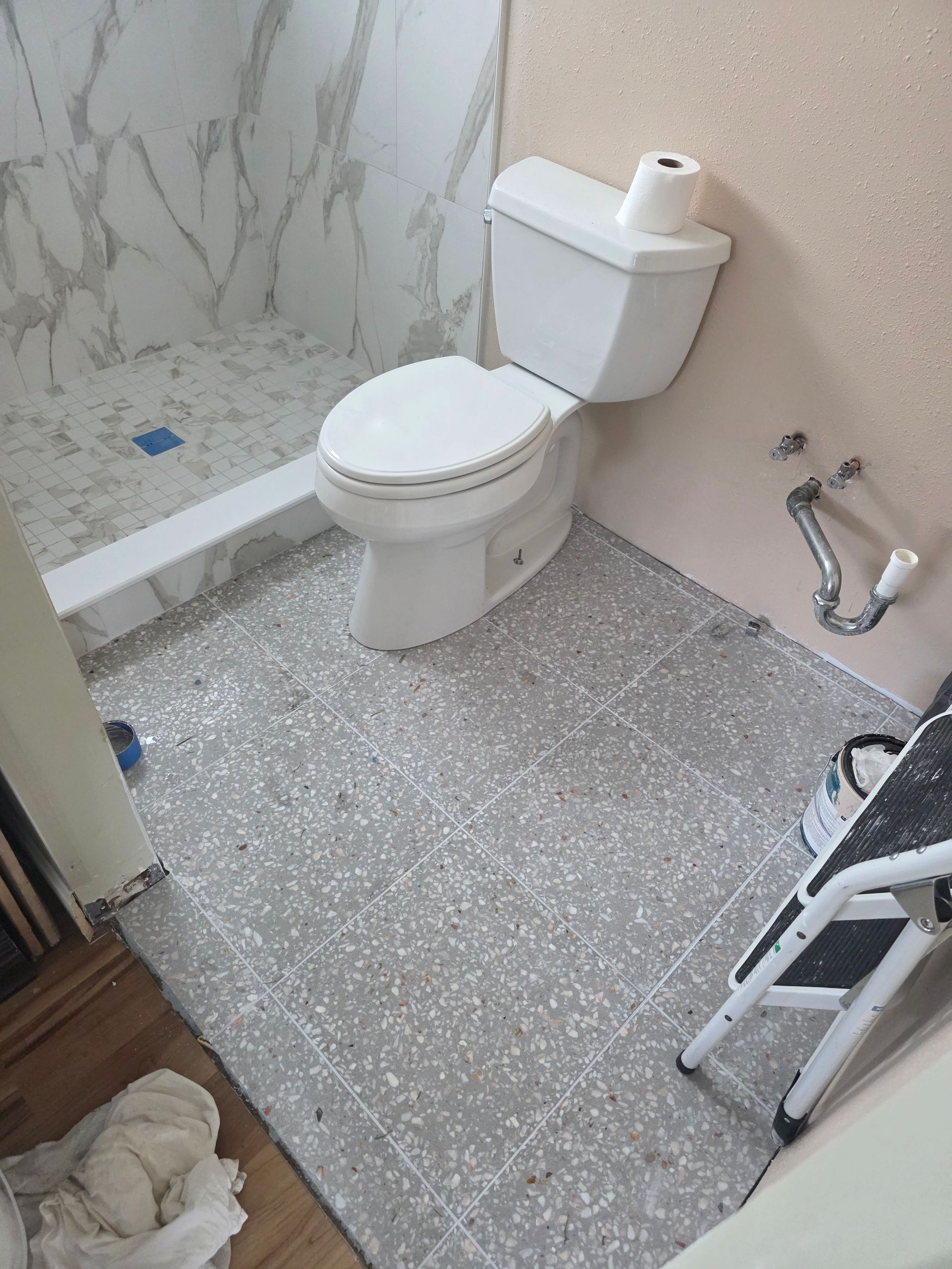 Bathroom with toilet, shower, and gray speckled flooring.