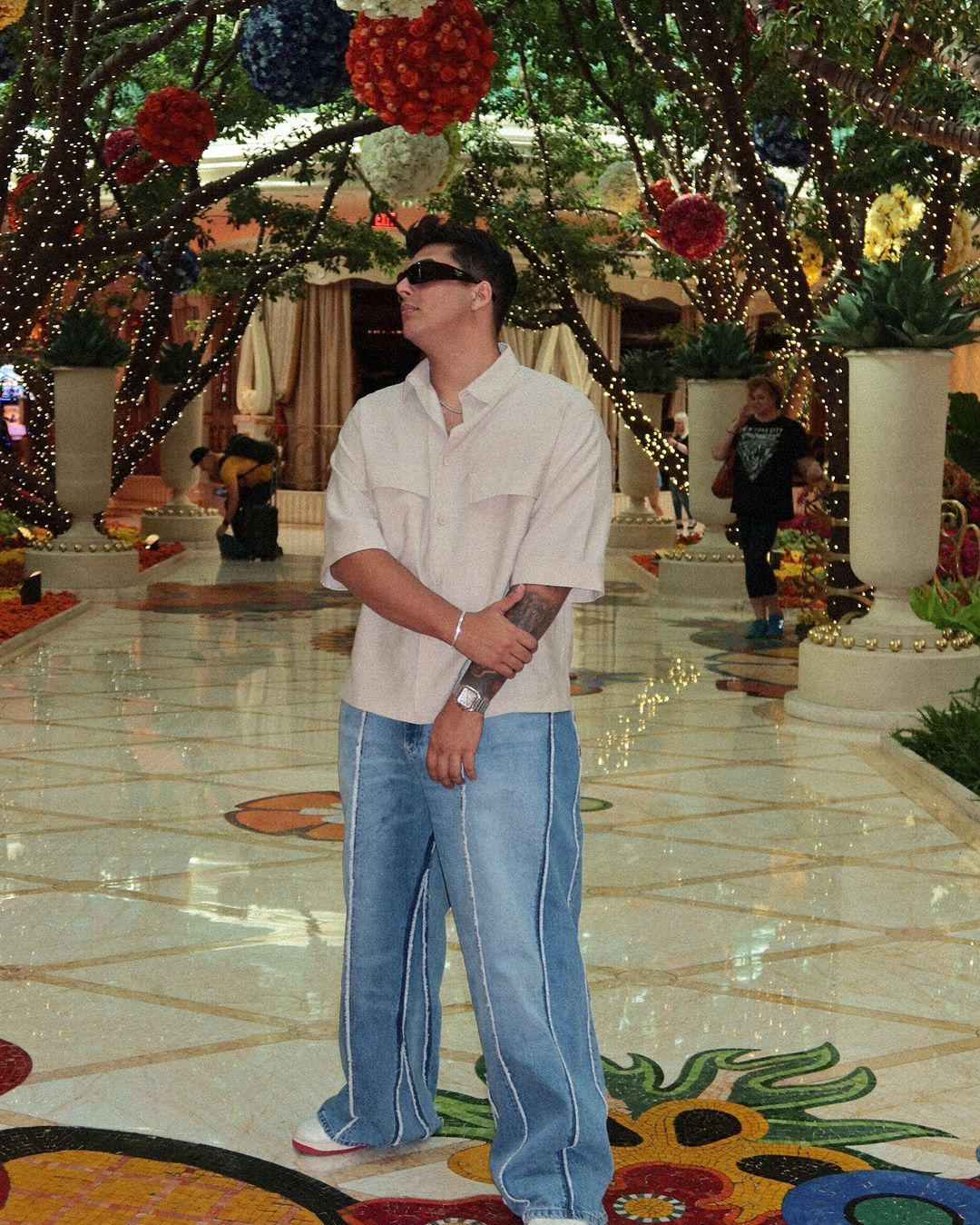 A man wearing sunglasses stands in front of a display of flowers
