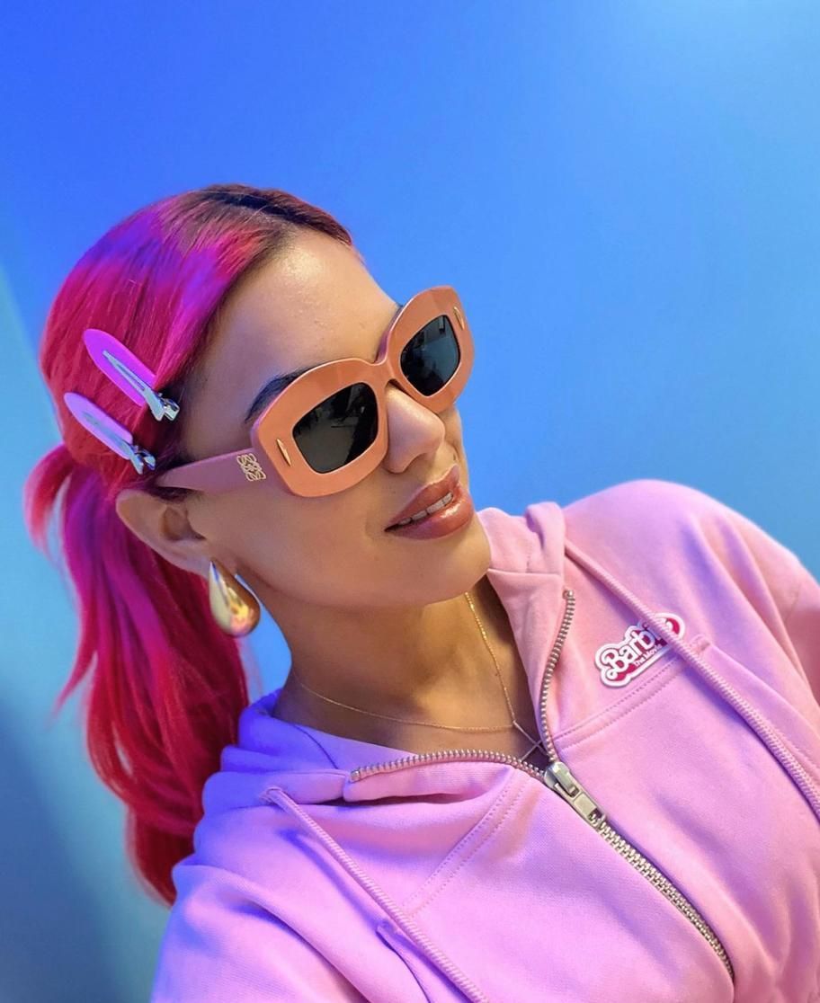 A woman with pink hair wearing sunglasses and a pink hoodie