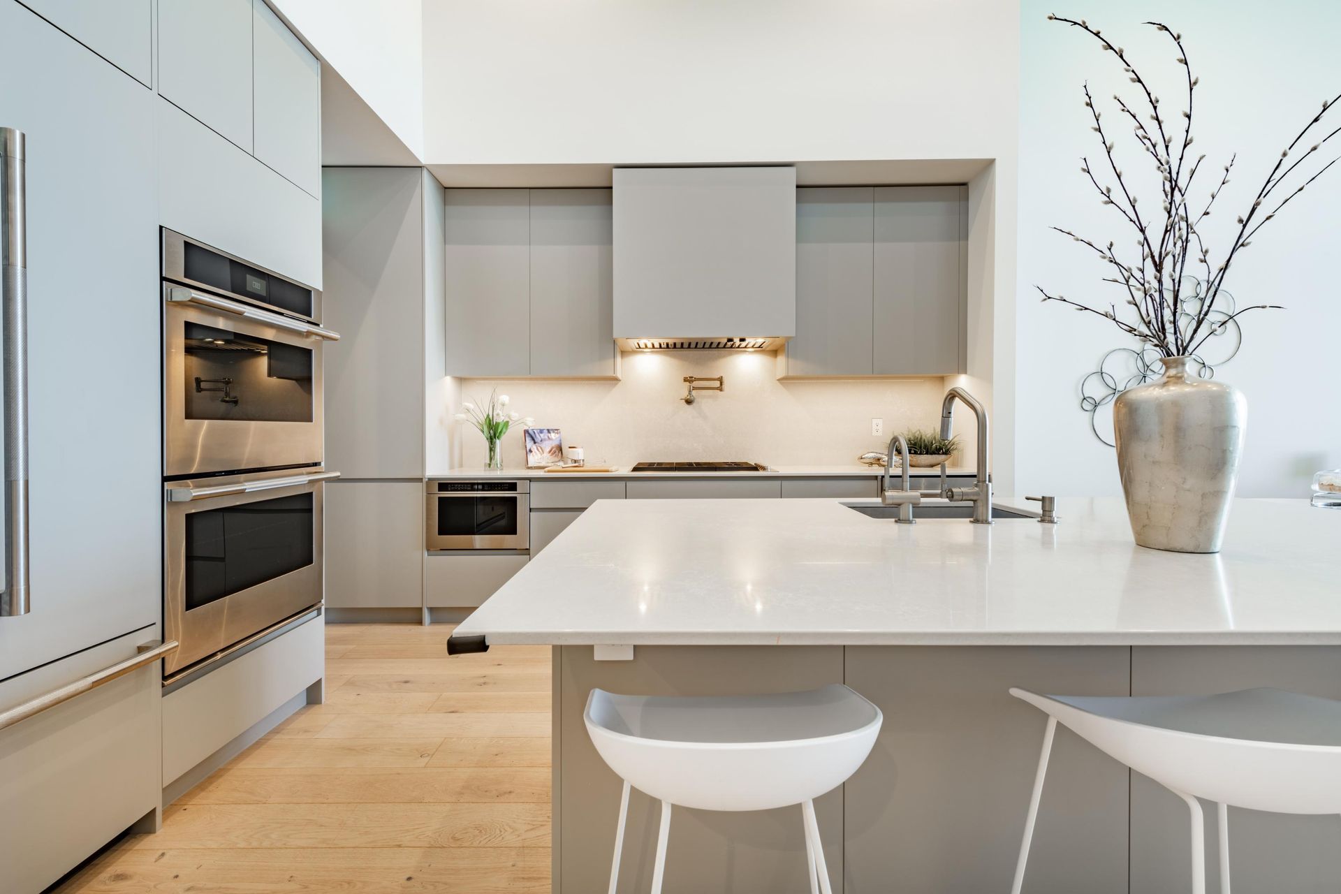 Modern white kitchen with island, built-in ovens, and a vase of branches on the counter
