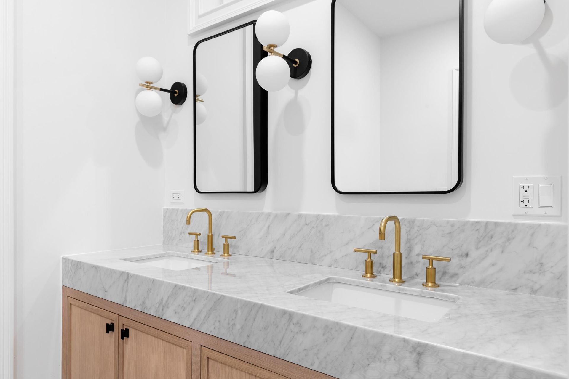 Modern bathroom vanity with marble countertop, brass faucets, and round wall sconces beside mirrored cabinets