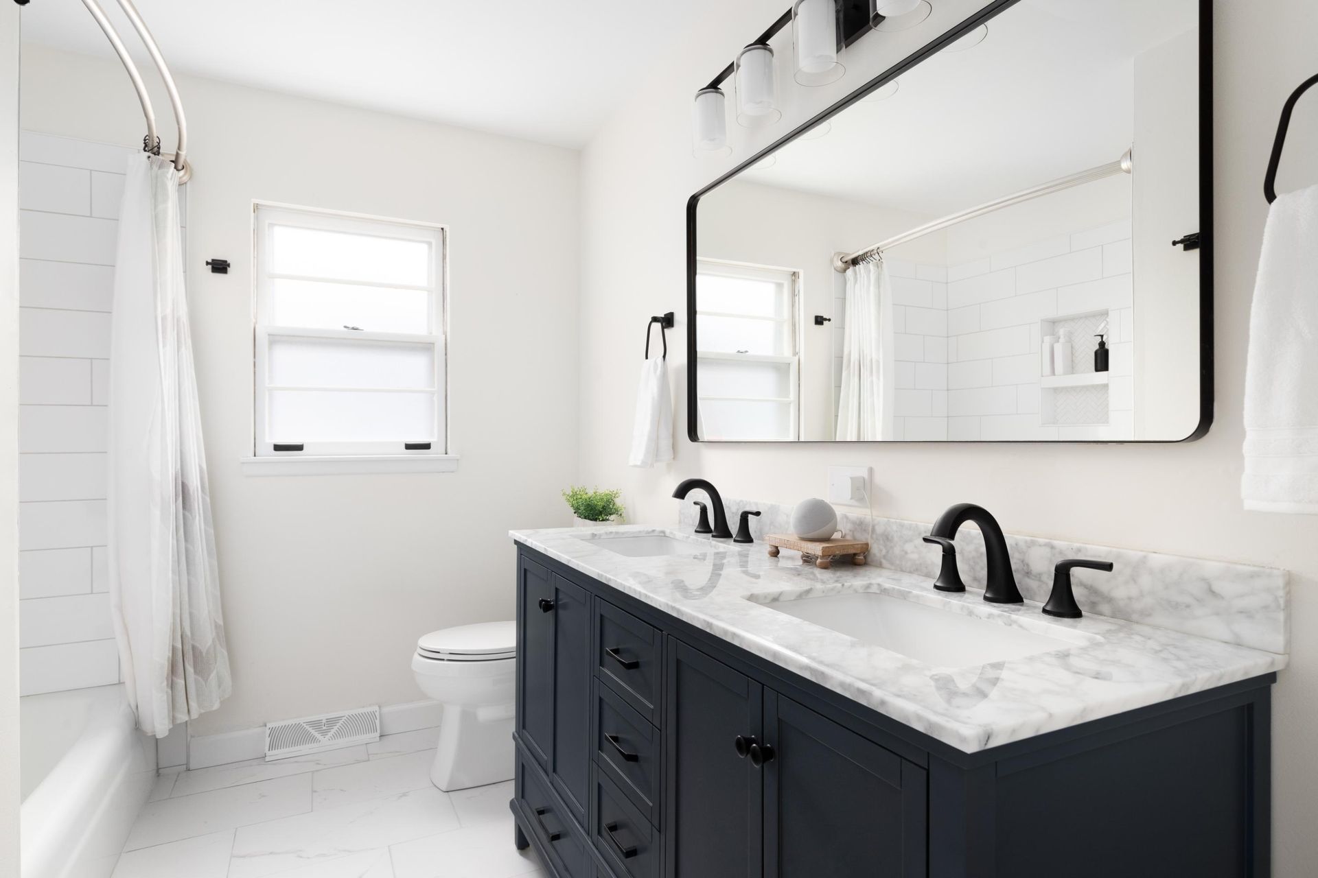 Bright white bathroom with black vanity, marble countertop, large mirror, shower curtain, and window.