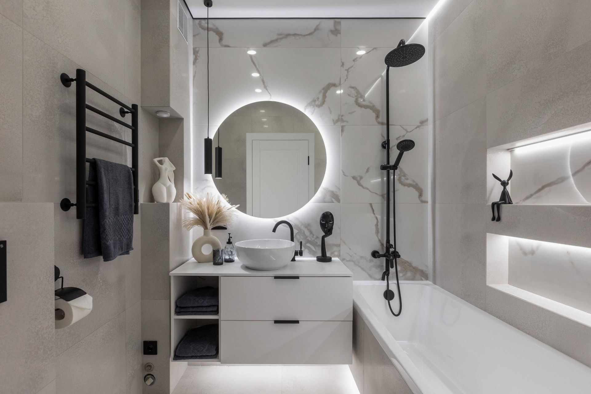 Modern white bathroom with round mirror, vanity, walk-in shower, and bathtub with wall niches