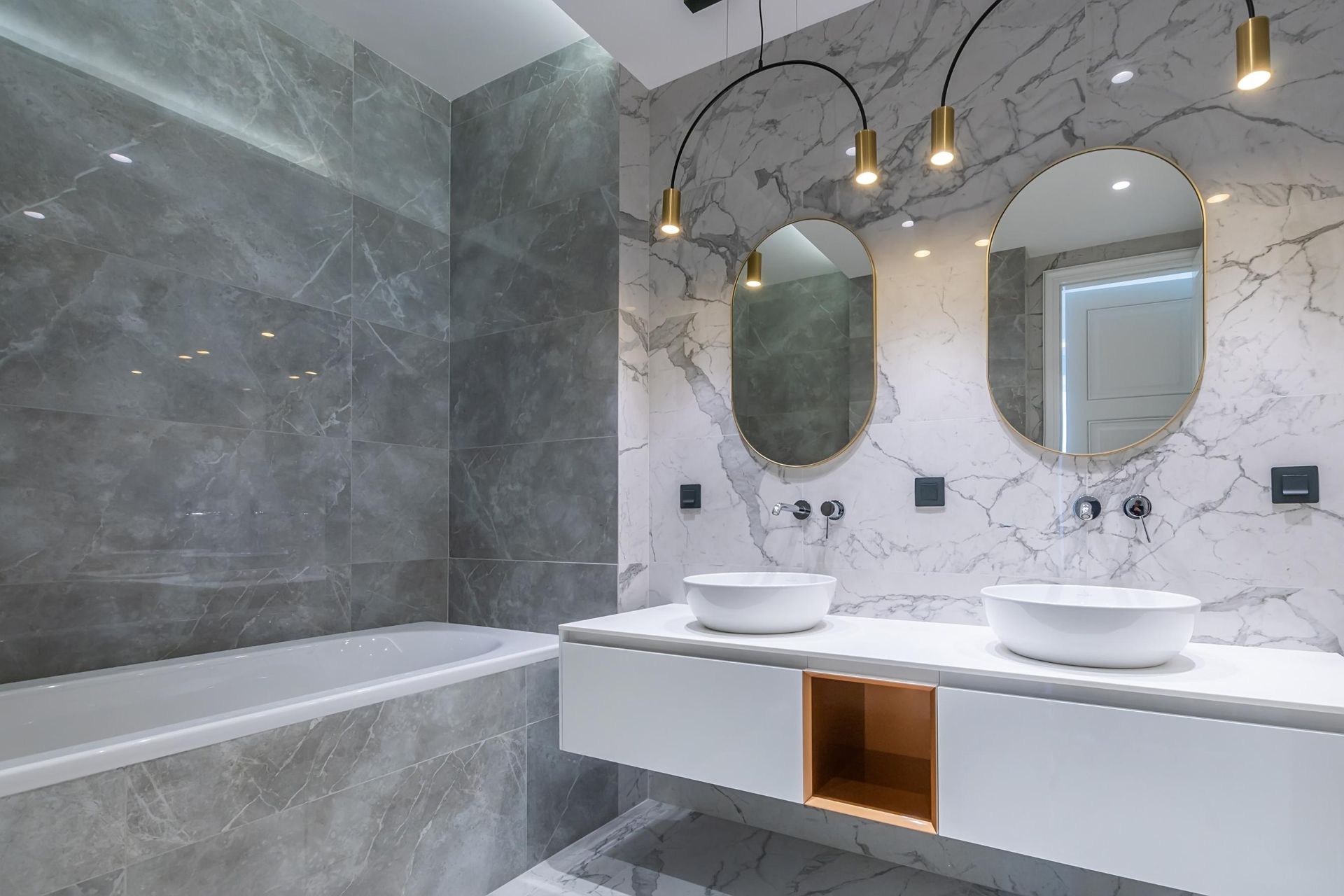 Modern bathroom with marble walls, double sinks, round mirrors, and a bathtub on the left