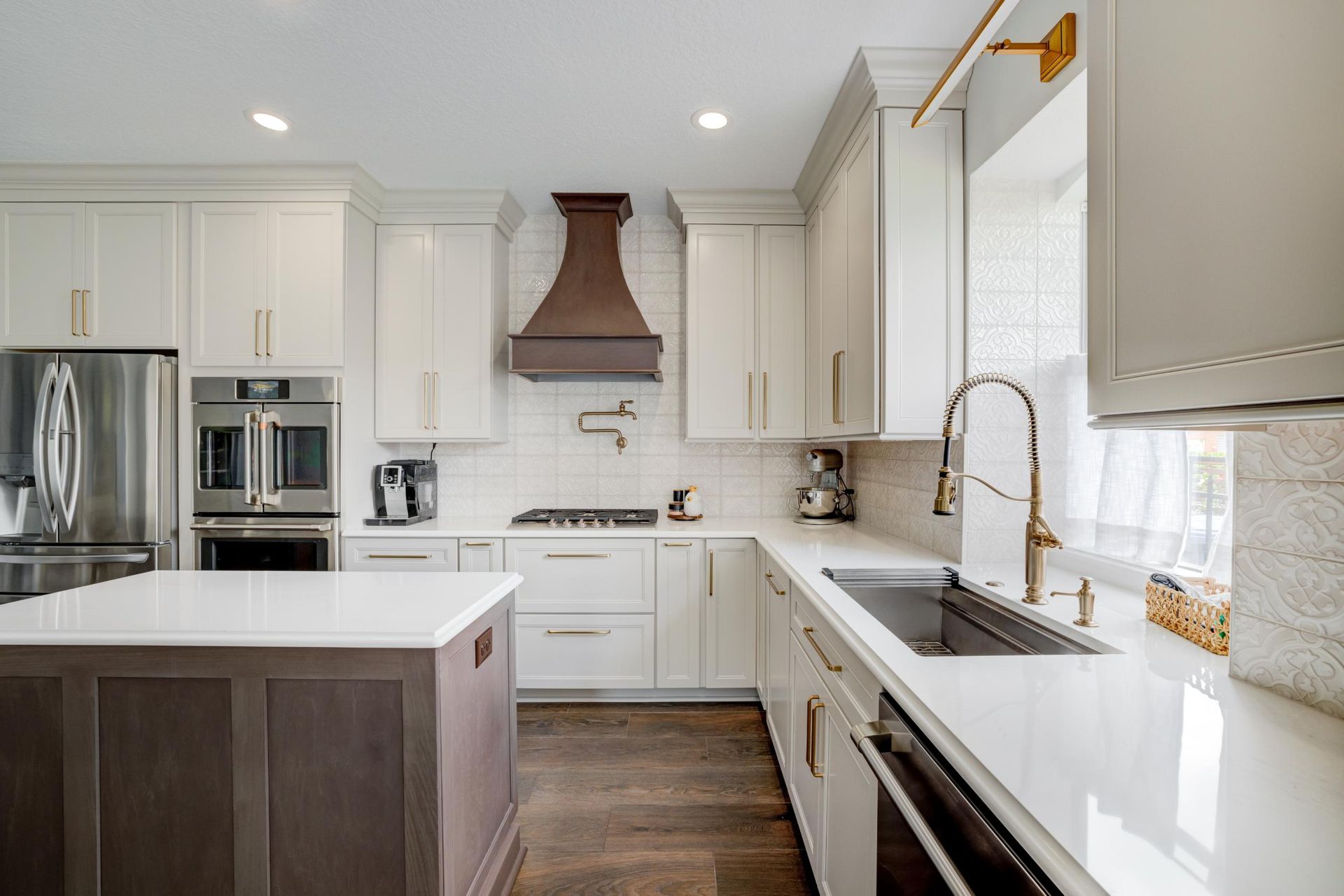 Bright modern white kitchen with island, stainless appliances, dark wood floors, and copper range hood