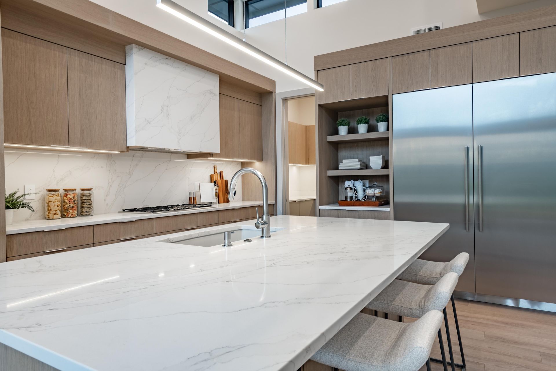 Modern kitchen with a large white island, wood cabinets, and stainless steel refrigerator