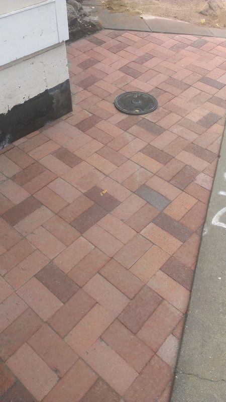 A brick walkway with a manhole cover in the middle of it.