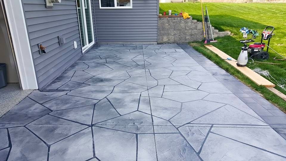 New gray concrete patio beside a house, with a lawn and garden tools in the background
