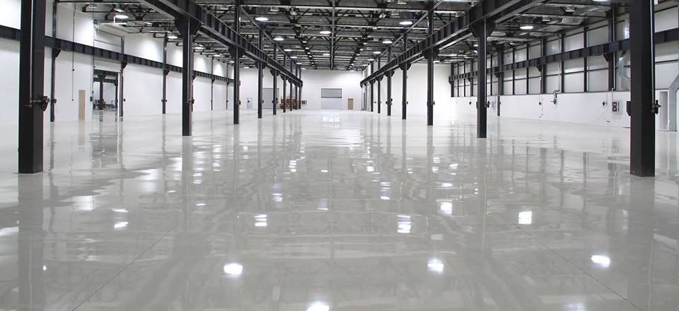 Empty industrial warehouse with polished concrete floor and rows of steel beams, lit by daylight