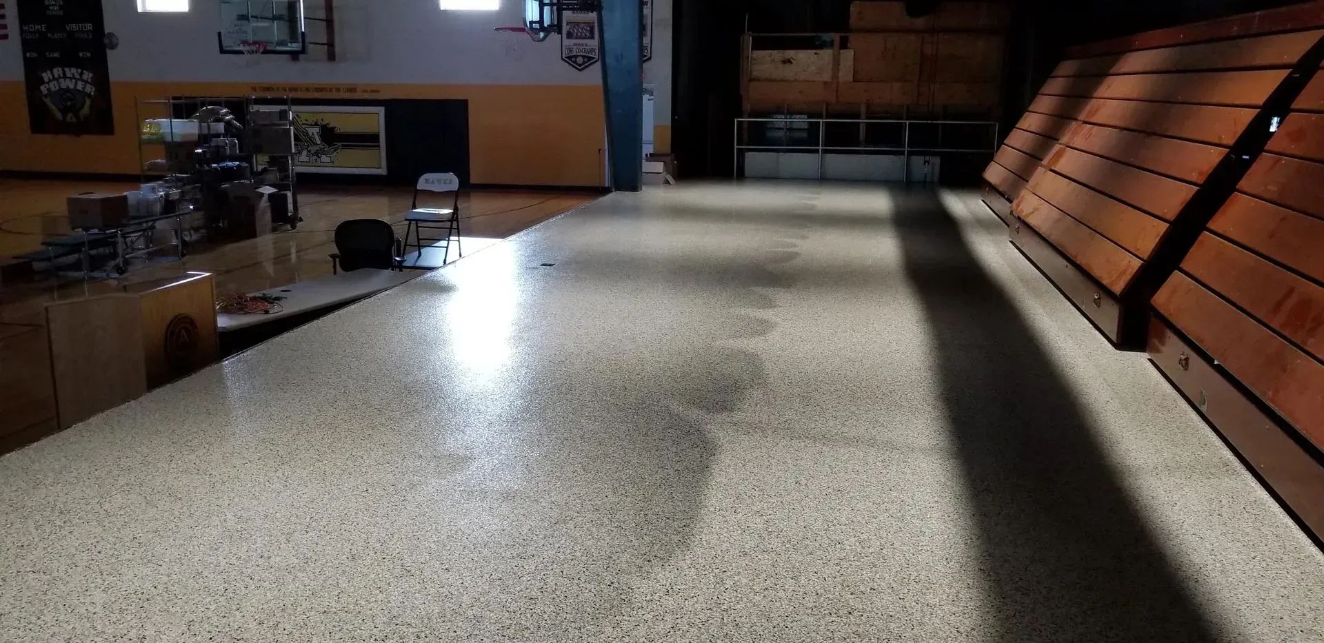 Empty indoor gym floor with wooden bleachers along the right side and tables in the back