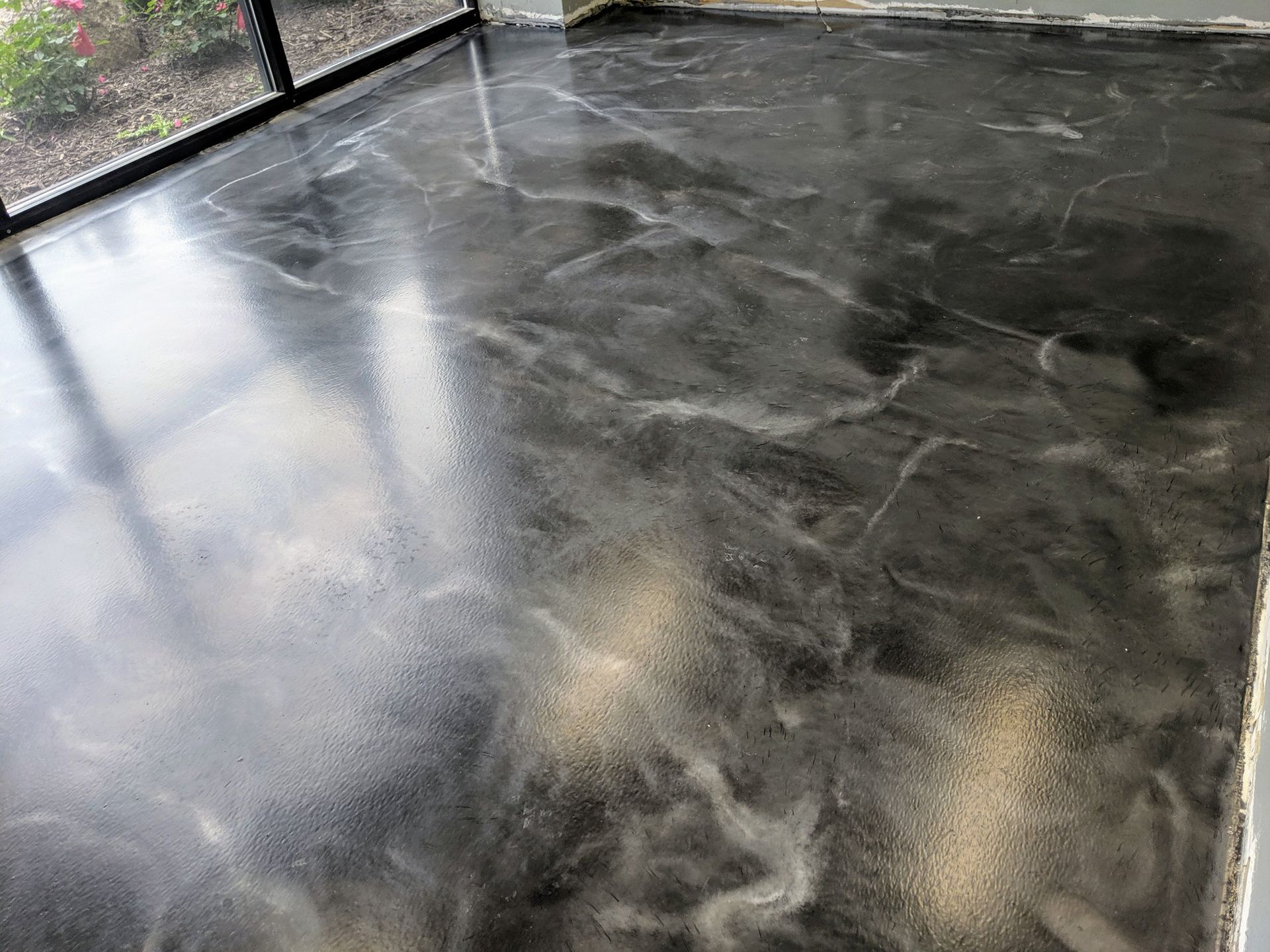 Shiny wet black concrete floor with reflections near a fence and wall