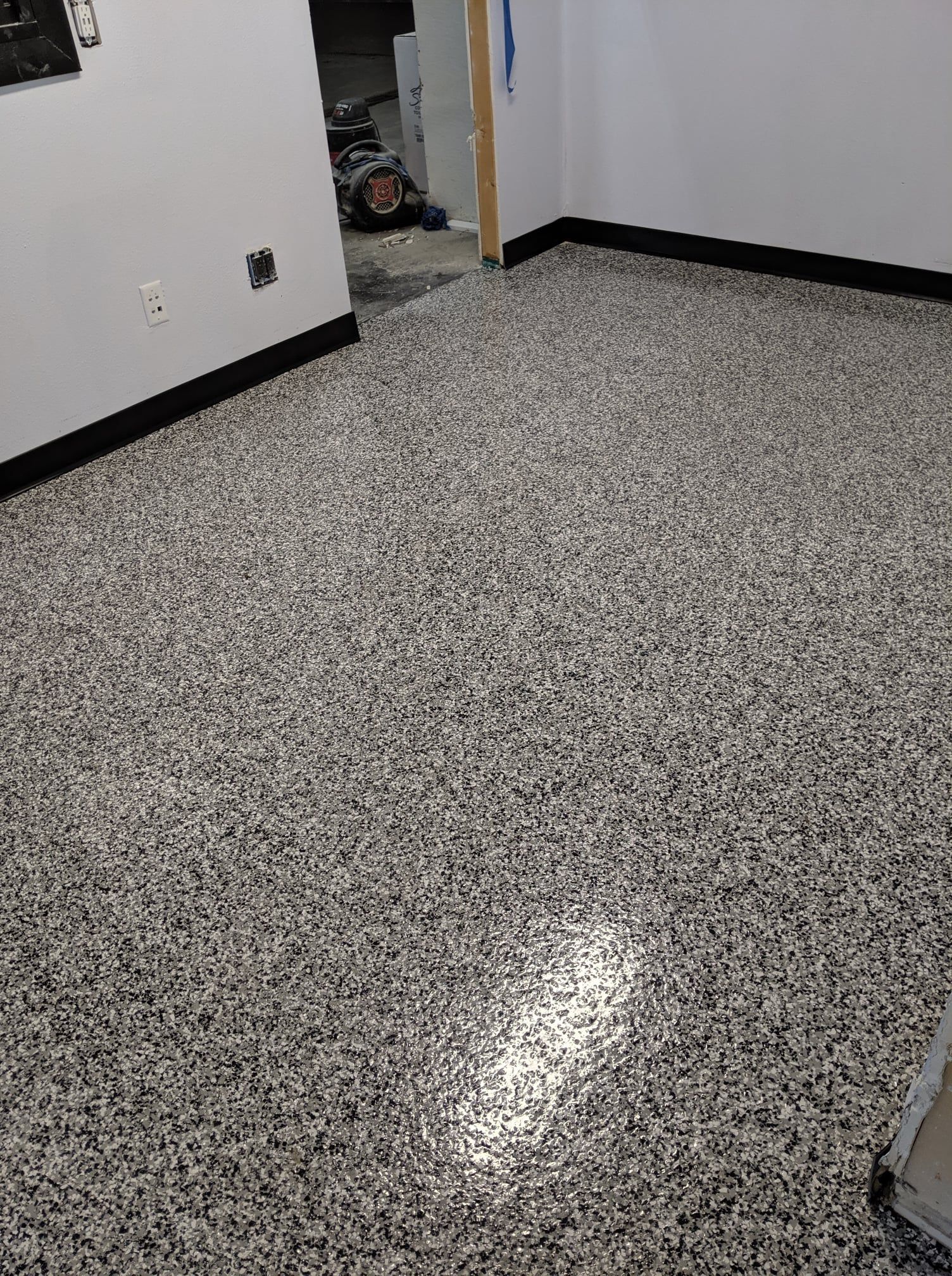 Empty room with speckled gray floor and white walls, viewed toward an open doorway.