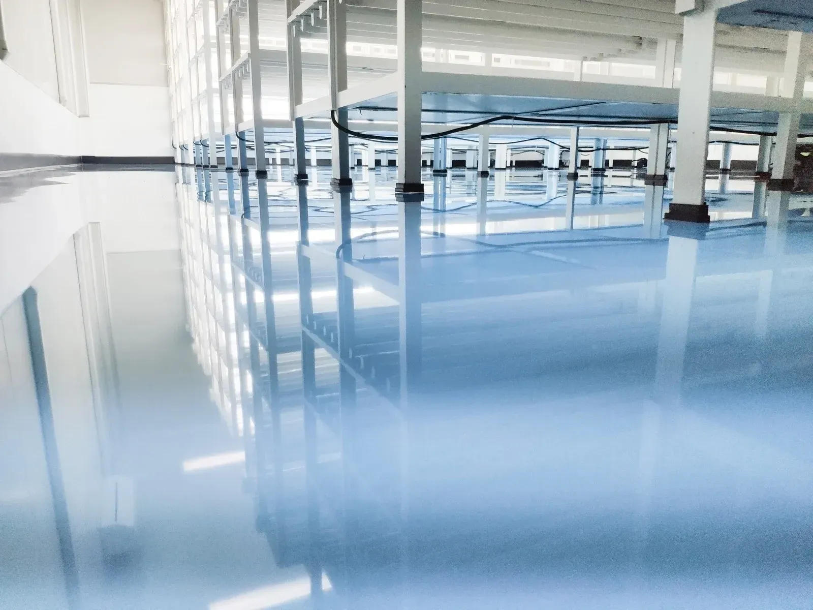 Empty bright warehouse with glossy blue floor and rows of metal worktables