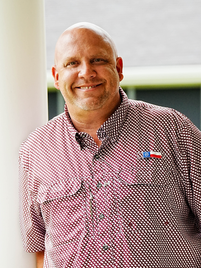 A man in a suit and red shirt is smiling for the camera.