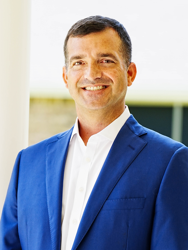 A man in a blue suit and white shirt is smiling for the camera.