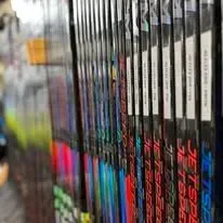 A row of hockey sticks are lined up on a shelf in a store.