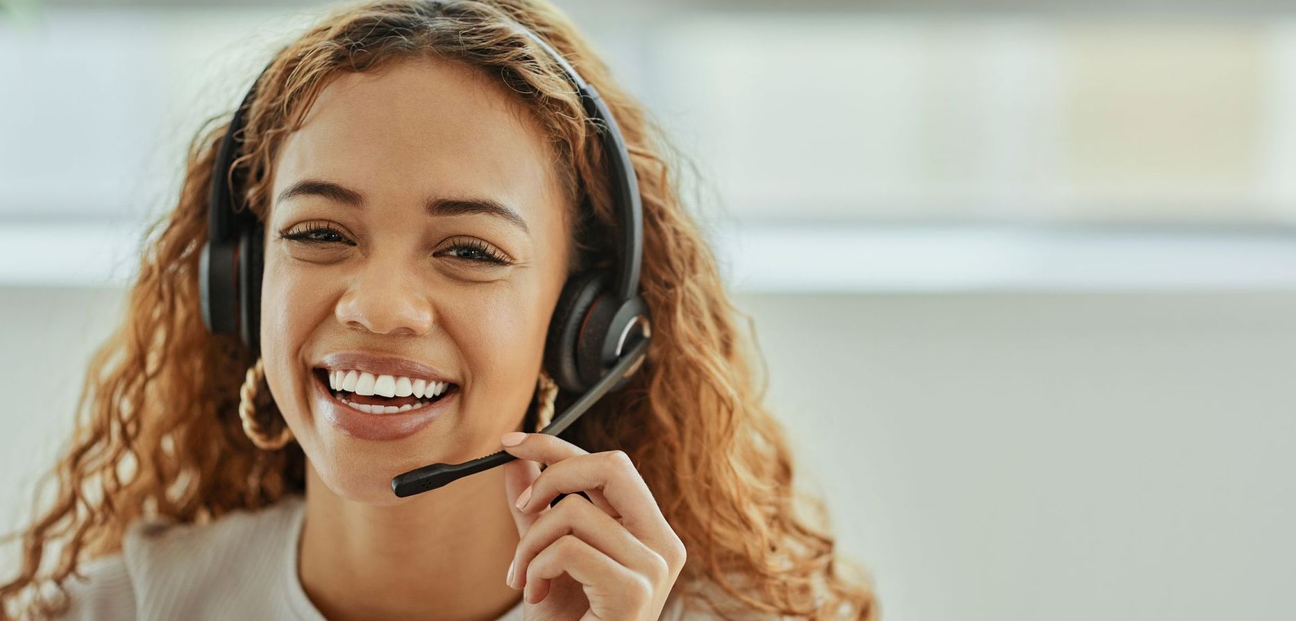 Smiling woman with curly hair wearing a headset, holding microphone.