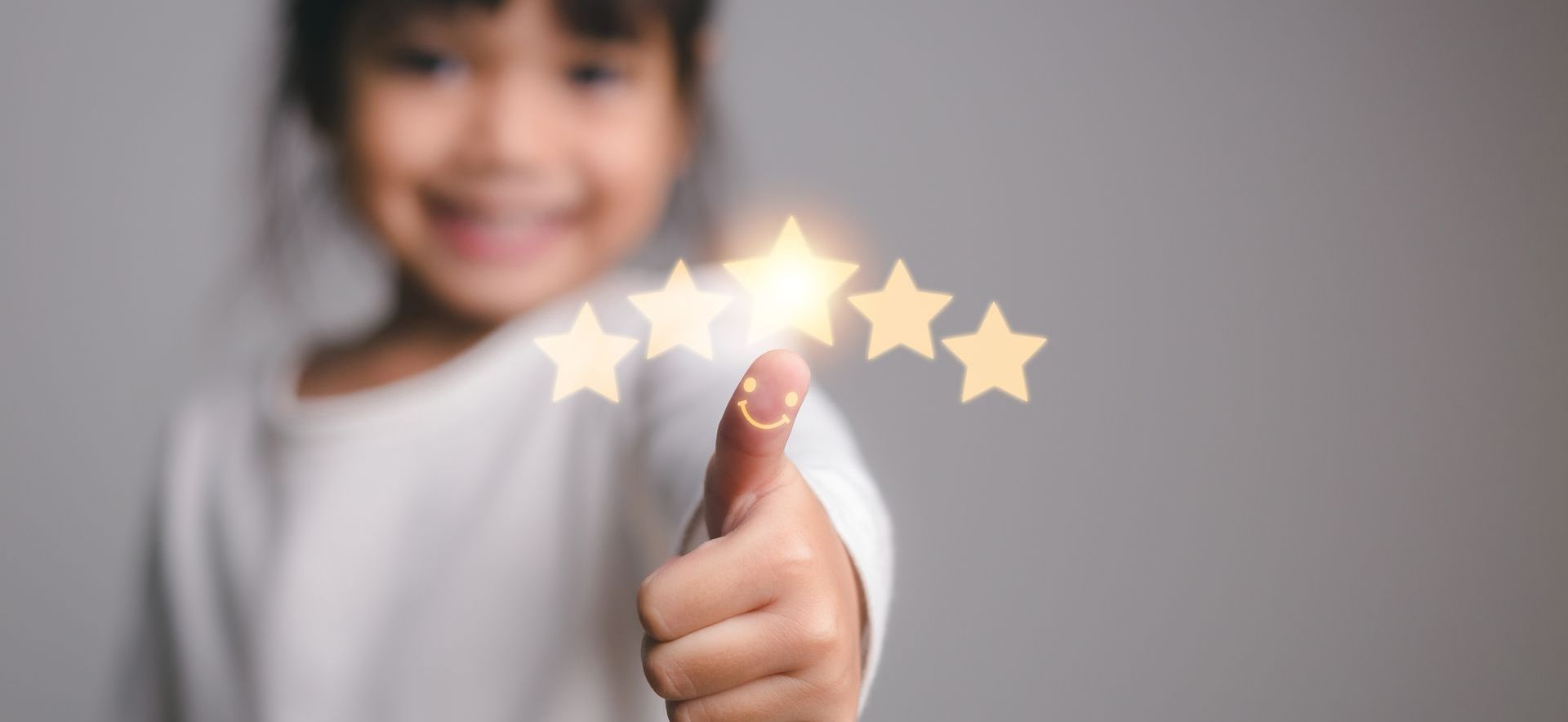 A child giving a thumbs-up with glowing stars, smiling, on a gray background.