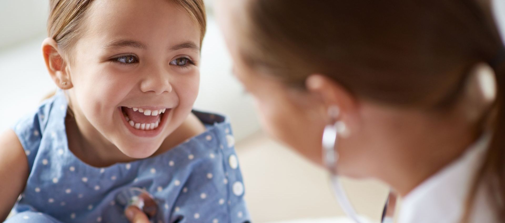 A smiling child being examined by a doctor with a stethoscope.