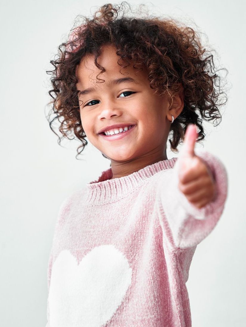 Child in pink sweater holding up a thumbs up sign