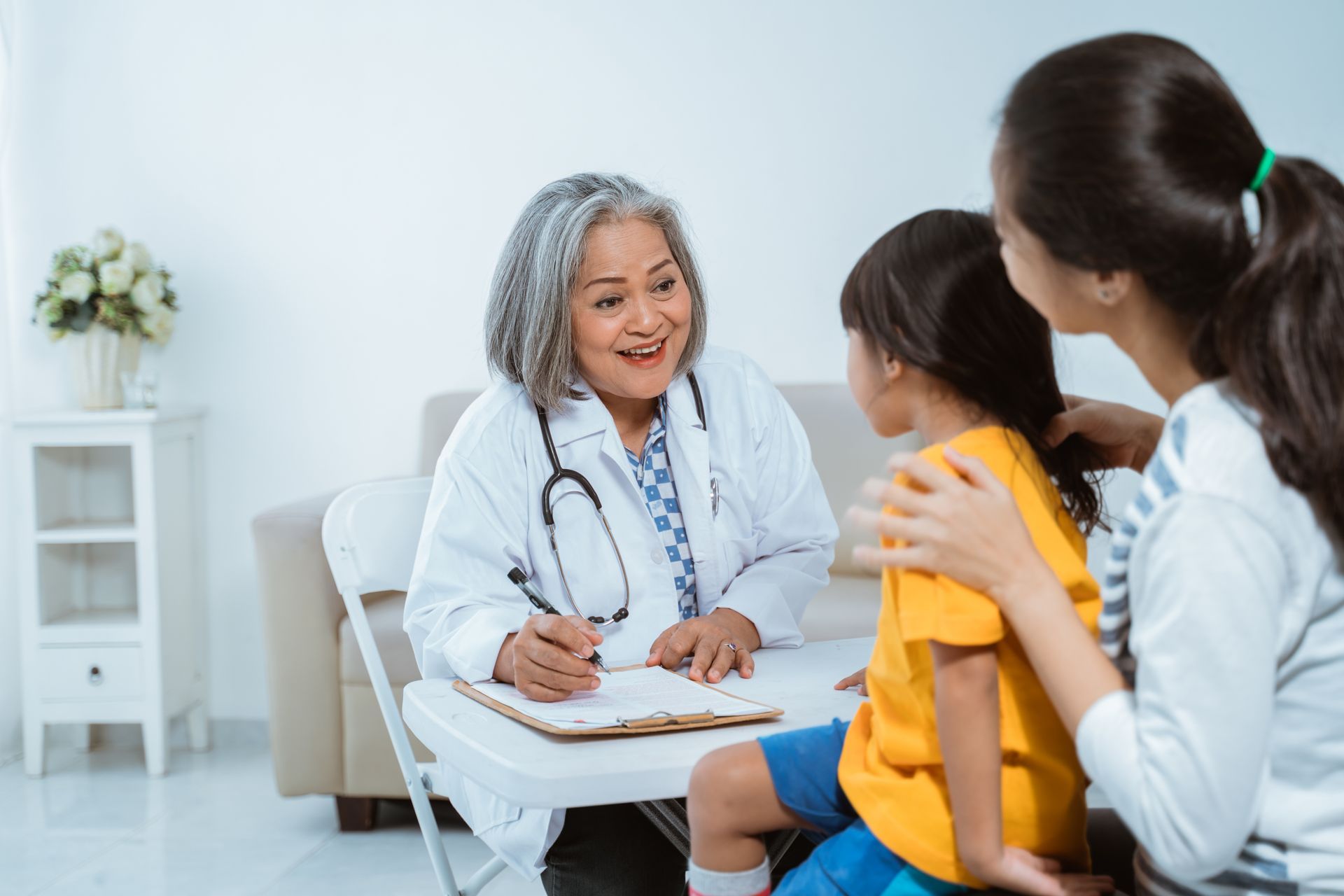 Doctor examining a young girl with her mother present, in a doctor's office.