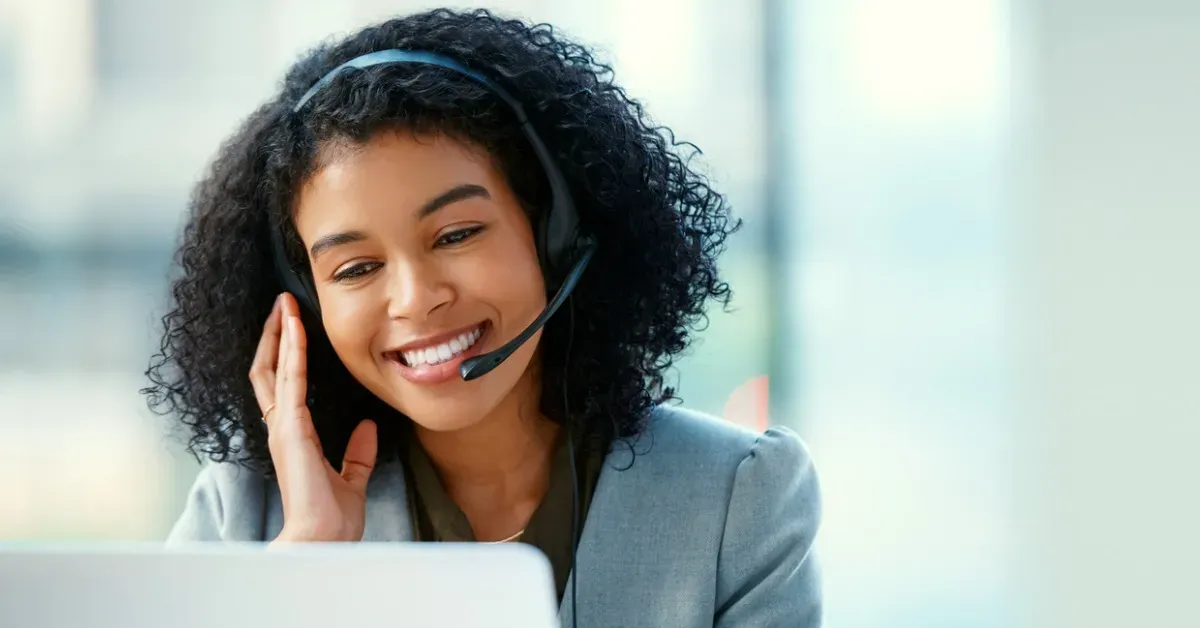 Smiling Black woman with headset working on laptop in office.