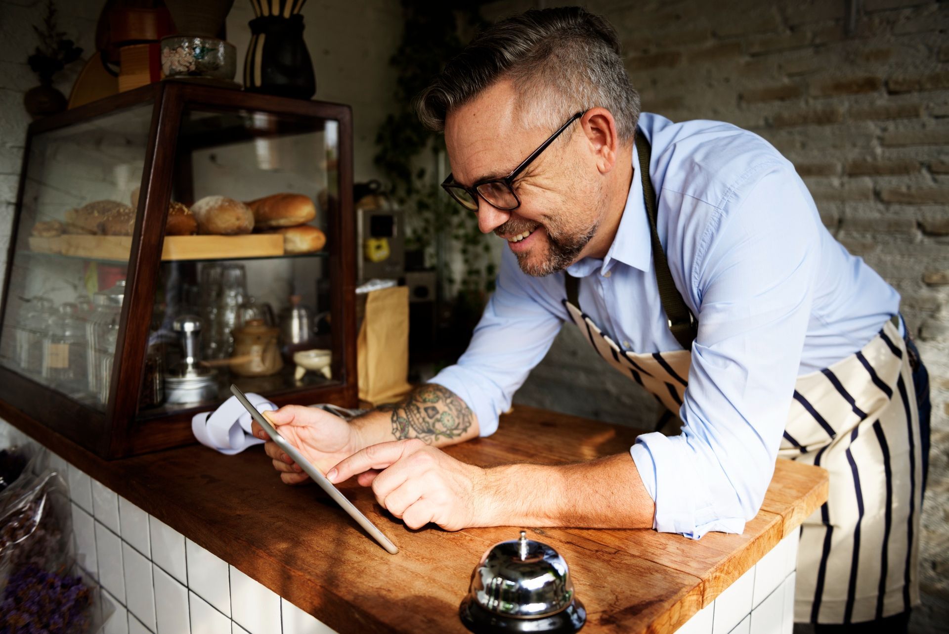 Man leaning over a wooden counter, using a phone in a rustic kitchen or workshop