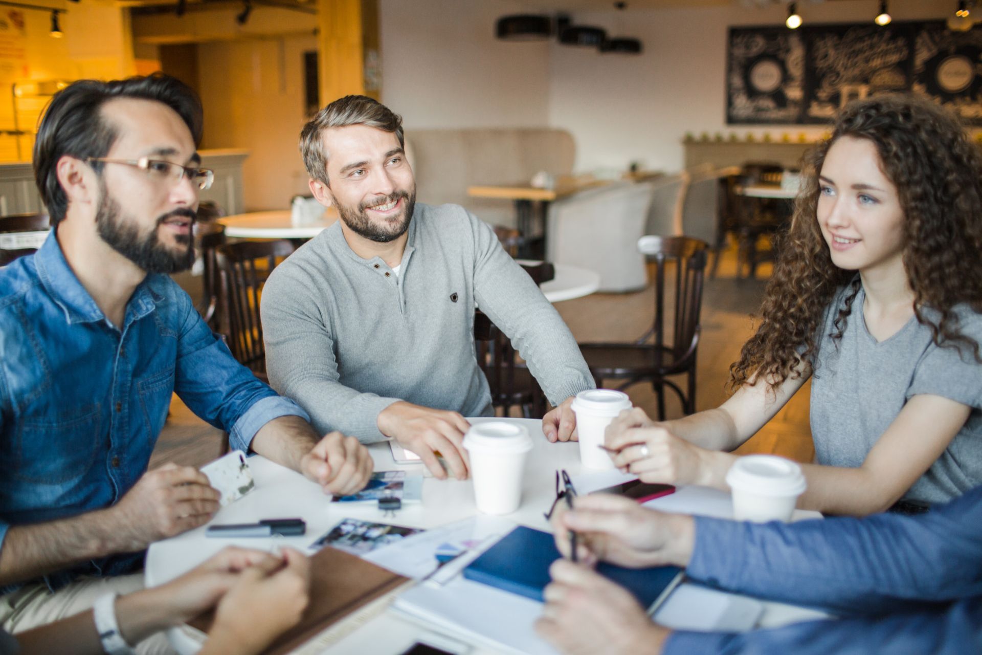 Small group in a meeting room discussing documents around a table with coffee mugs.