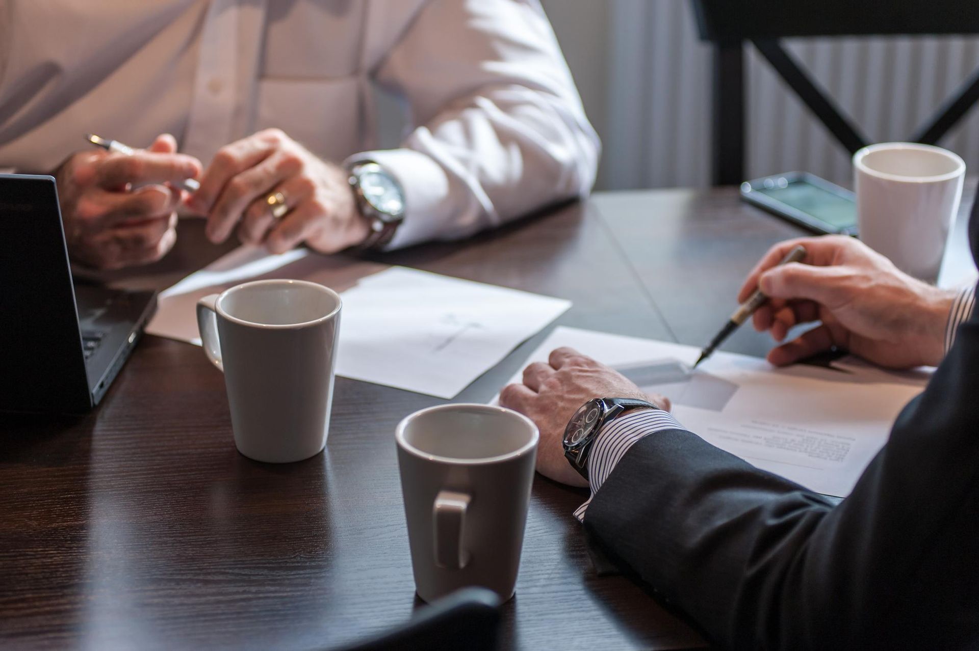 People in business attire discussing documents at a conference table with coffee mugs and a laptop