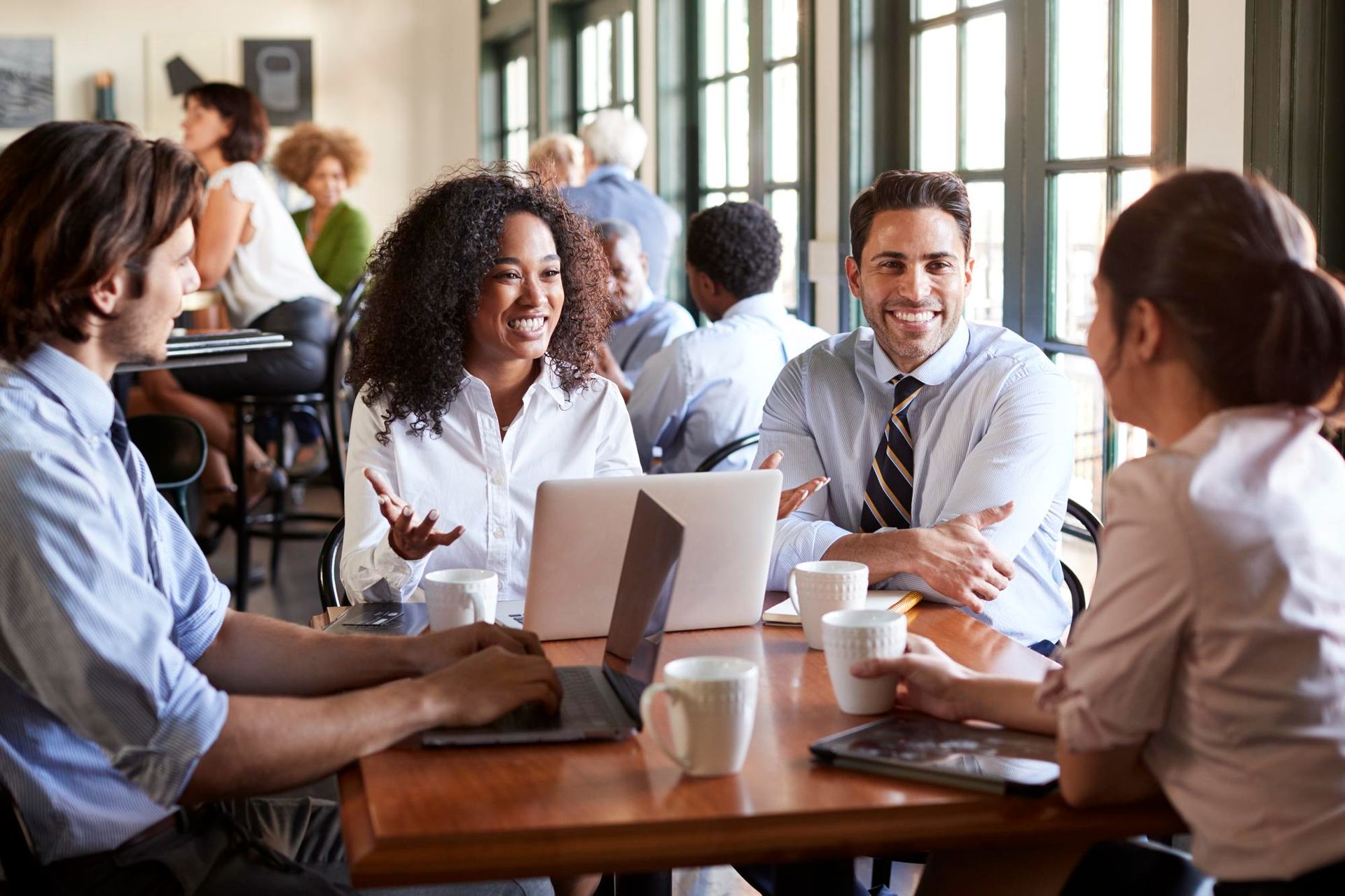 Colleagues chatting around a conference table with laptops and coffee in a bright office meeting room