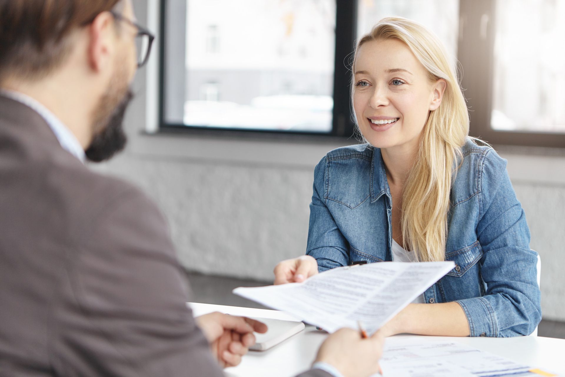Two people discussing documents at a table in a bright office, with one smiling and holding papers.