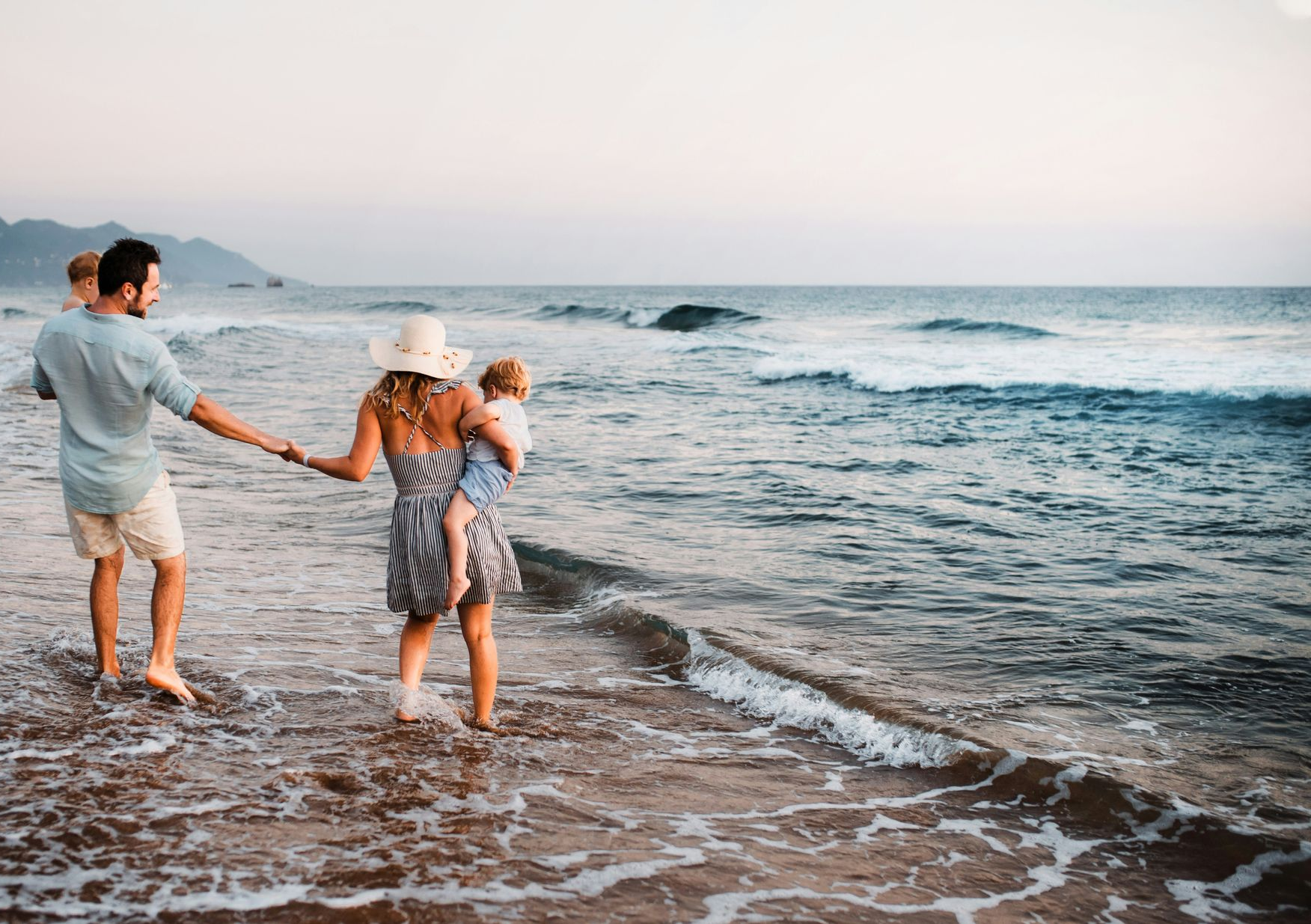 Three people holding hands while walking along a sandy beach at sunset