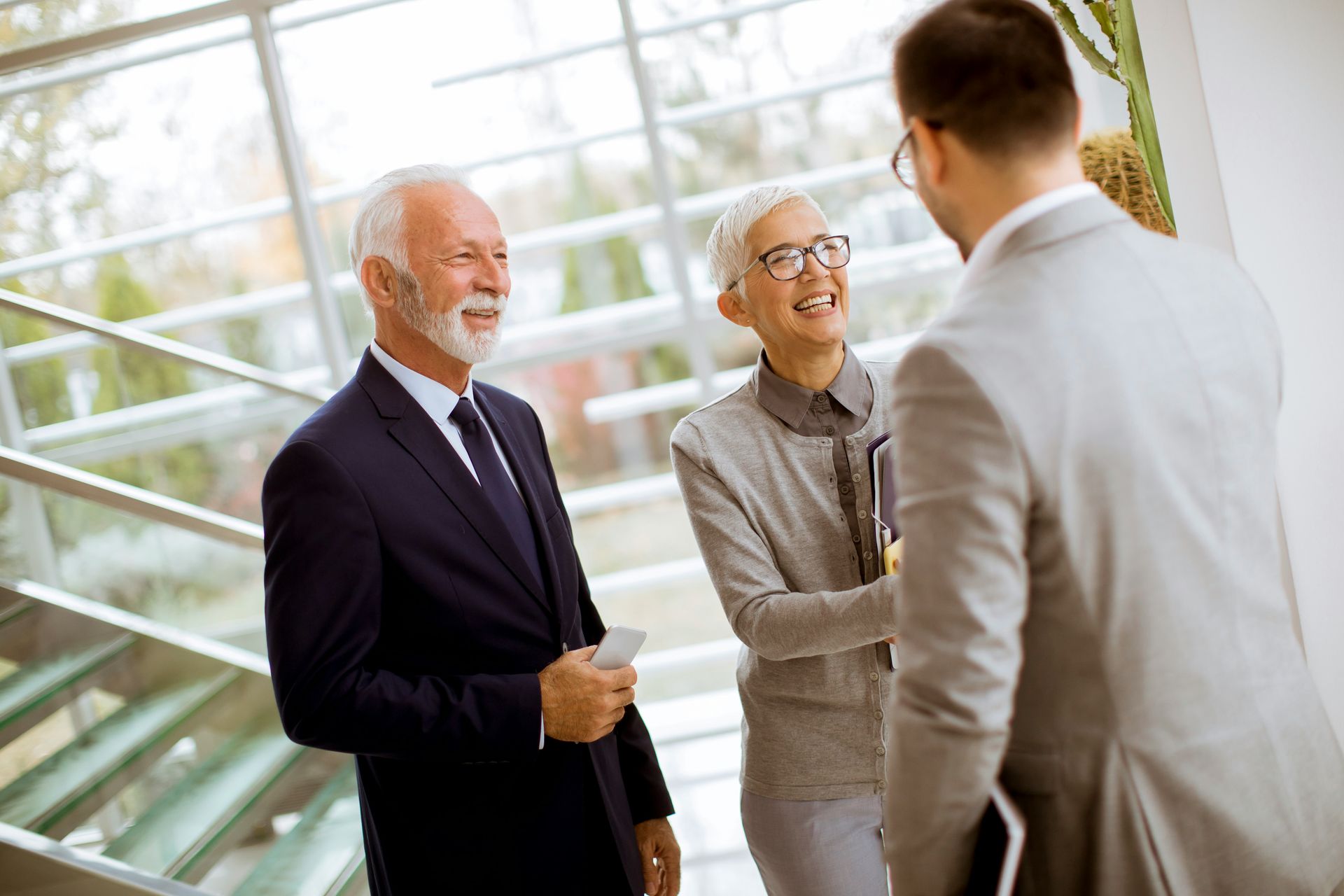 Three businesspeople smiling and talking in a bright office lobby