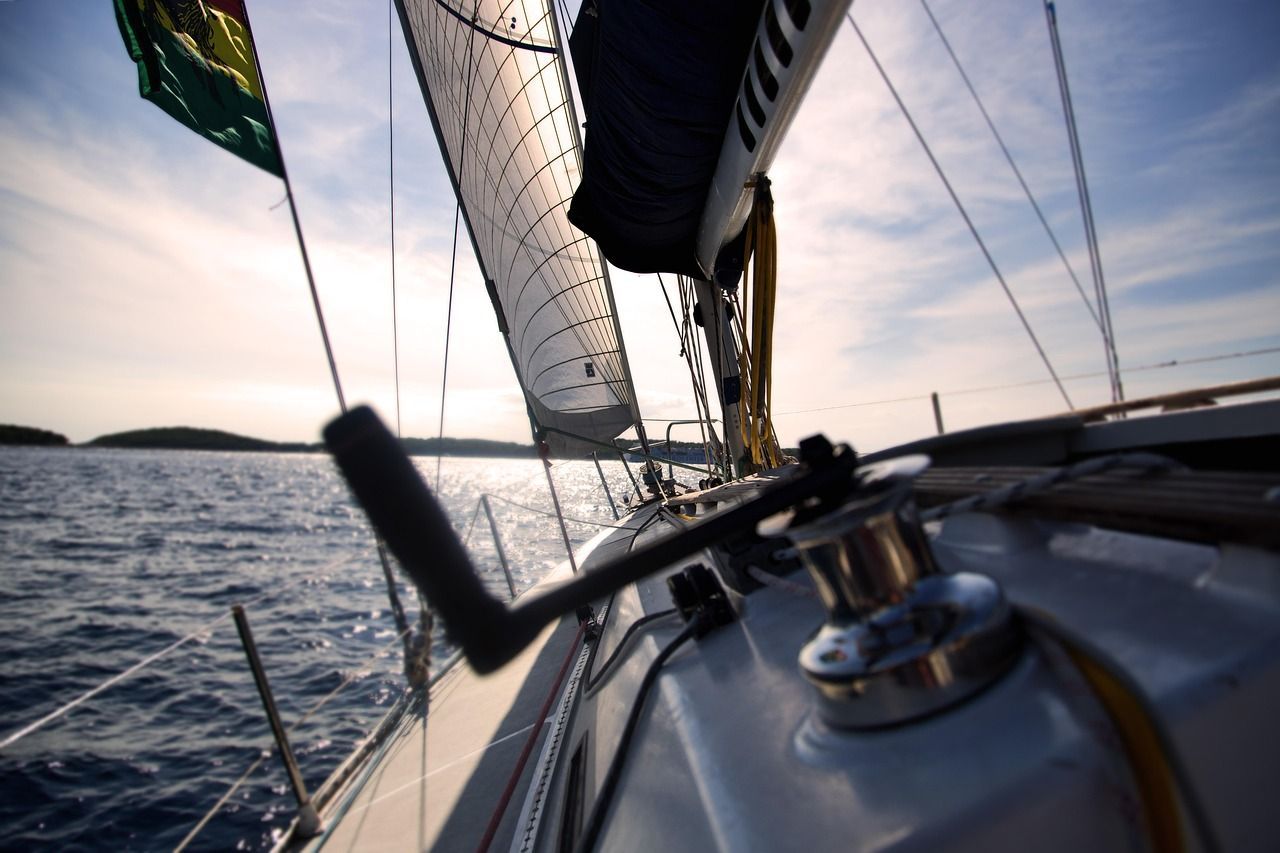 Sailing boat deck and rigging at sea, with sails up and a calm horizon at sunset