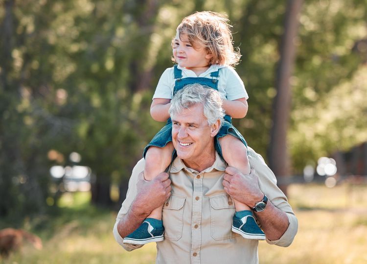 Older man carrying a small child on his shoulders in a sunlit park